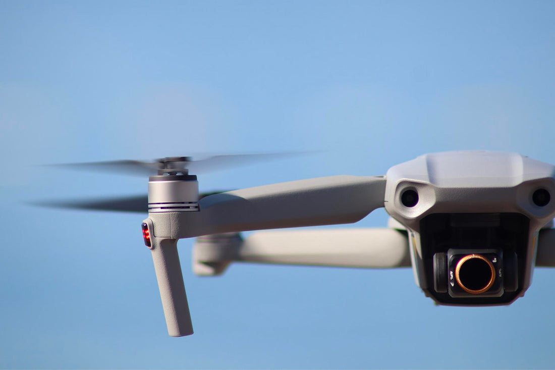 Close-up of a drone with spinning propellers and camera against a clear blue sky.