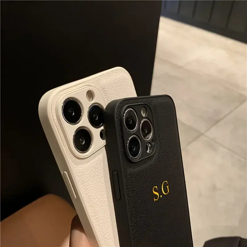 Close-up of two personalized iPhone cases in white and black leather, featuring initials on the black case.