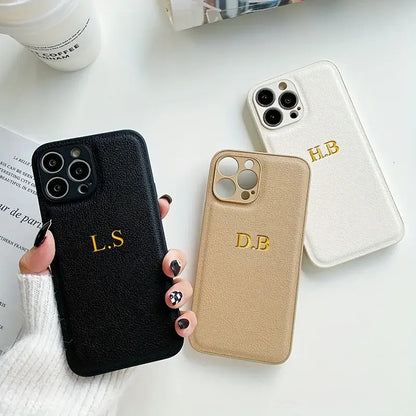 Three personalized leather iPhone cases in black, beige, and white with initials L.S, D.B, and H.B, displayed on a table.